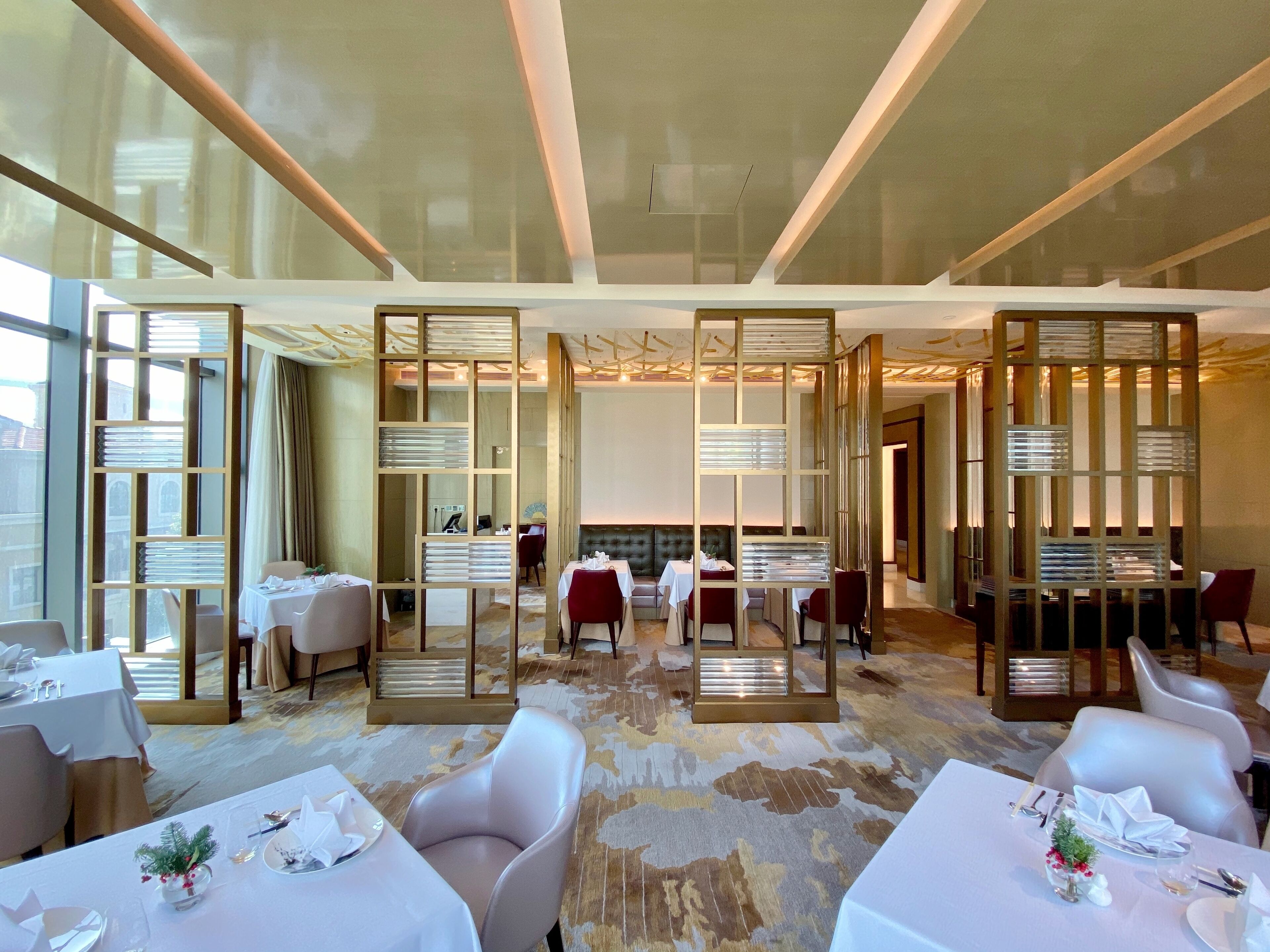 A modern hotel dining area with tables set for guests, a large window, and a decorative partition.