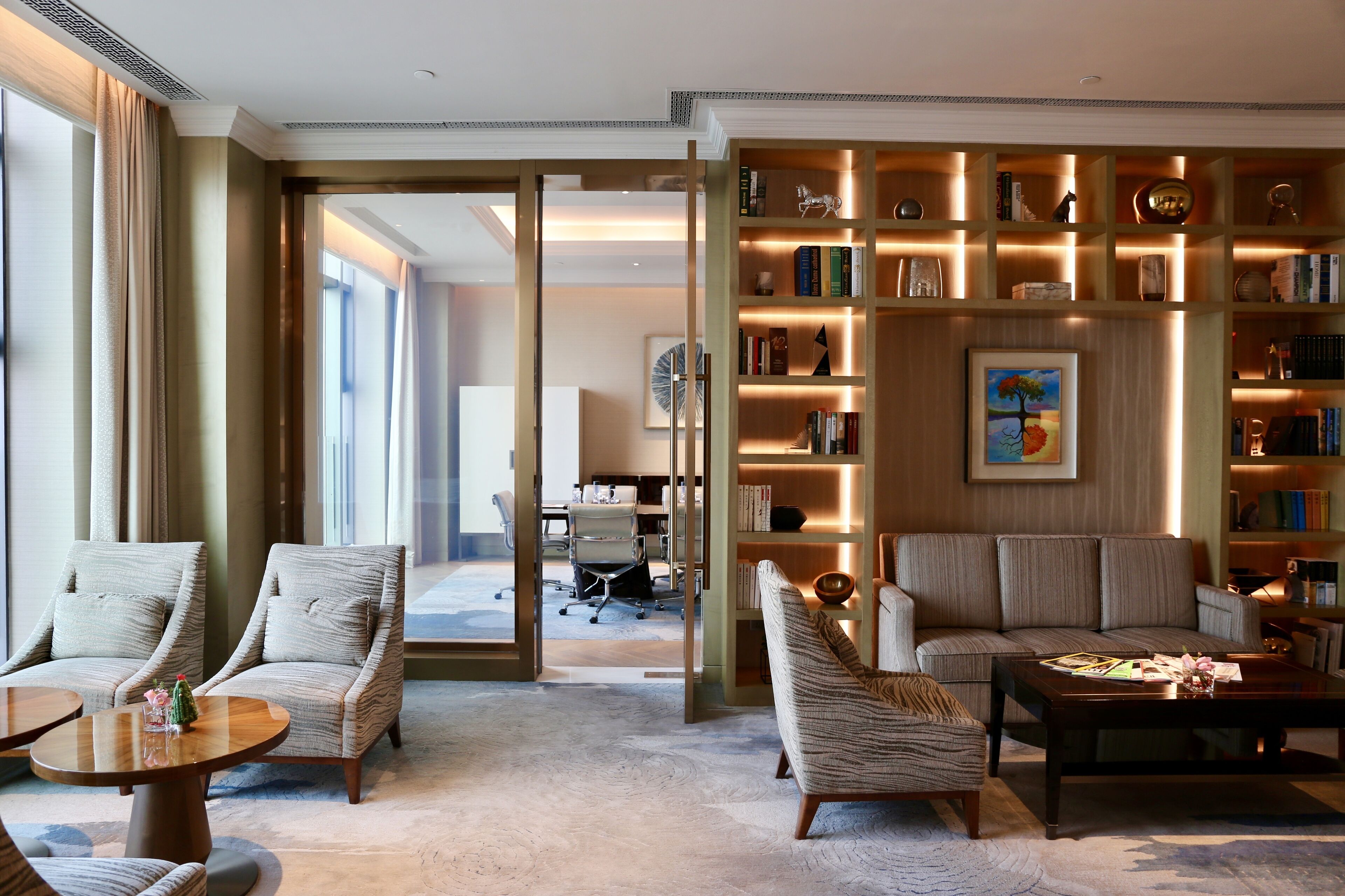 A spacious living room with a large bookshelf, comfortable seating, and a view into another room.