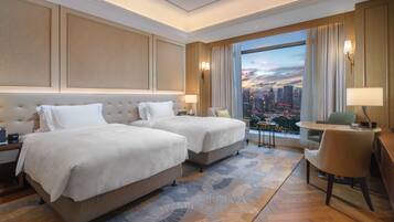 Habitación de hotel con dos camas, un escritorio, una silla y vistas a la ciudad.