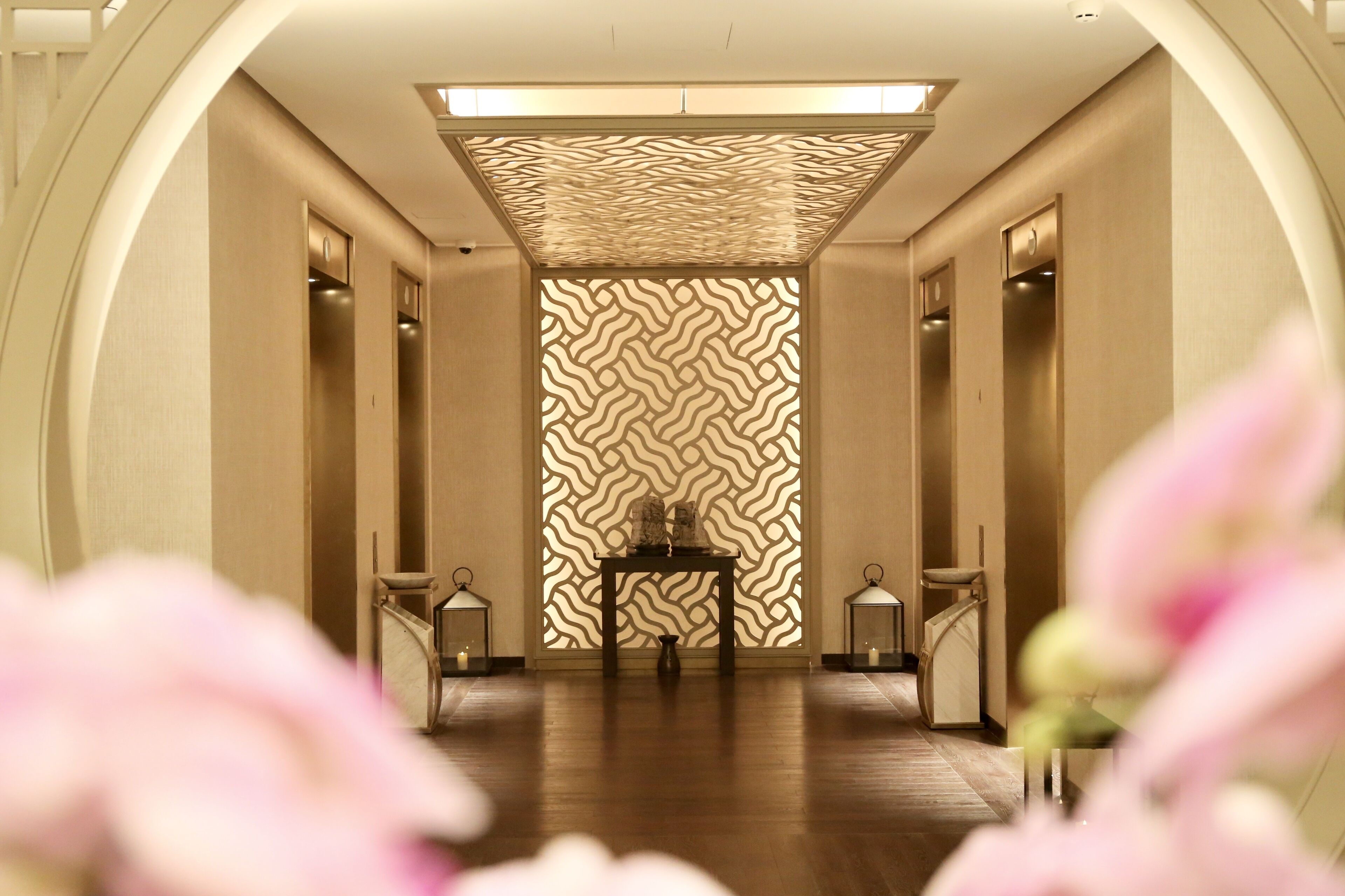 A hallway with a patterned wall, a central table, and two lanterns on either side.