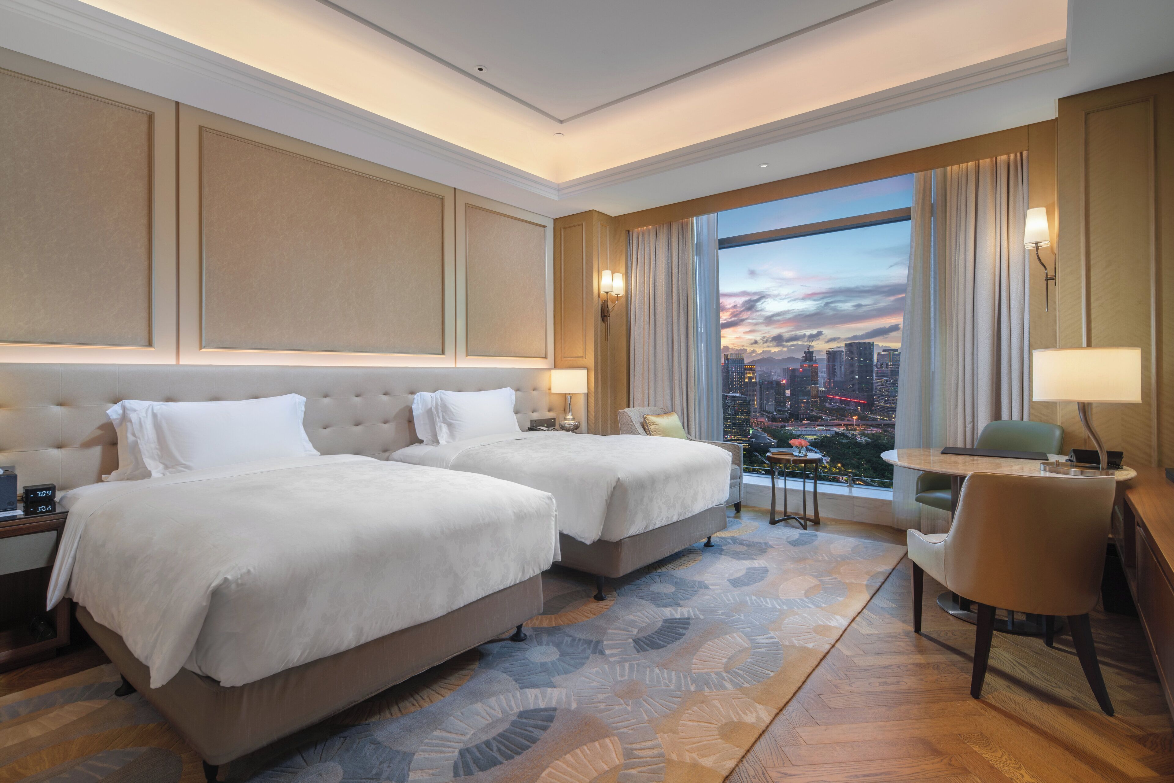 Habitación de hotel con dos camas, un escritorio, una silla y vistas a la ciudad.