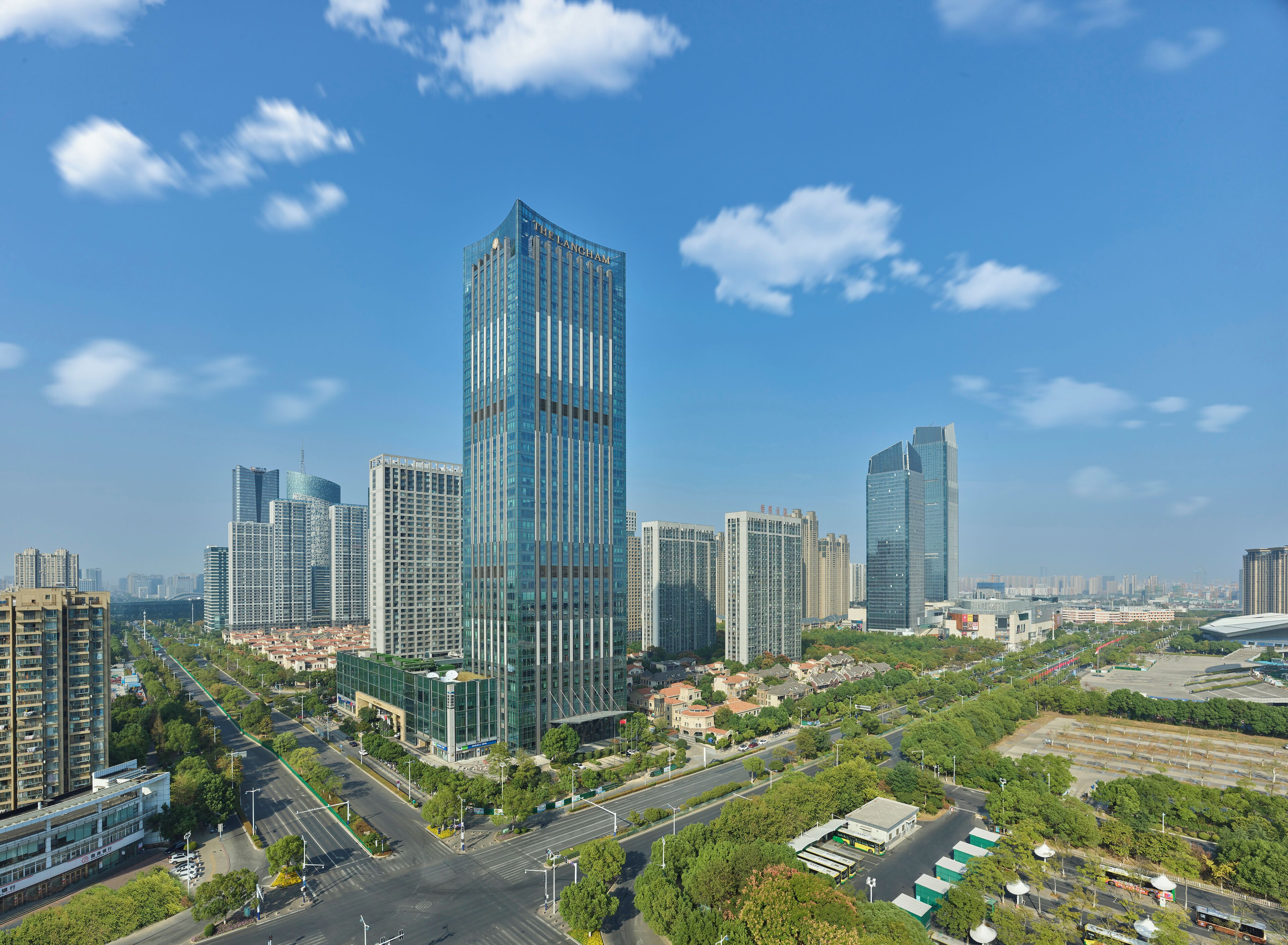 A high-rise hotel with a modern glass facade, surrounded by other high-rise buildings and a mix of greenery and urban infrastructure.