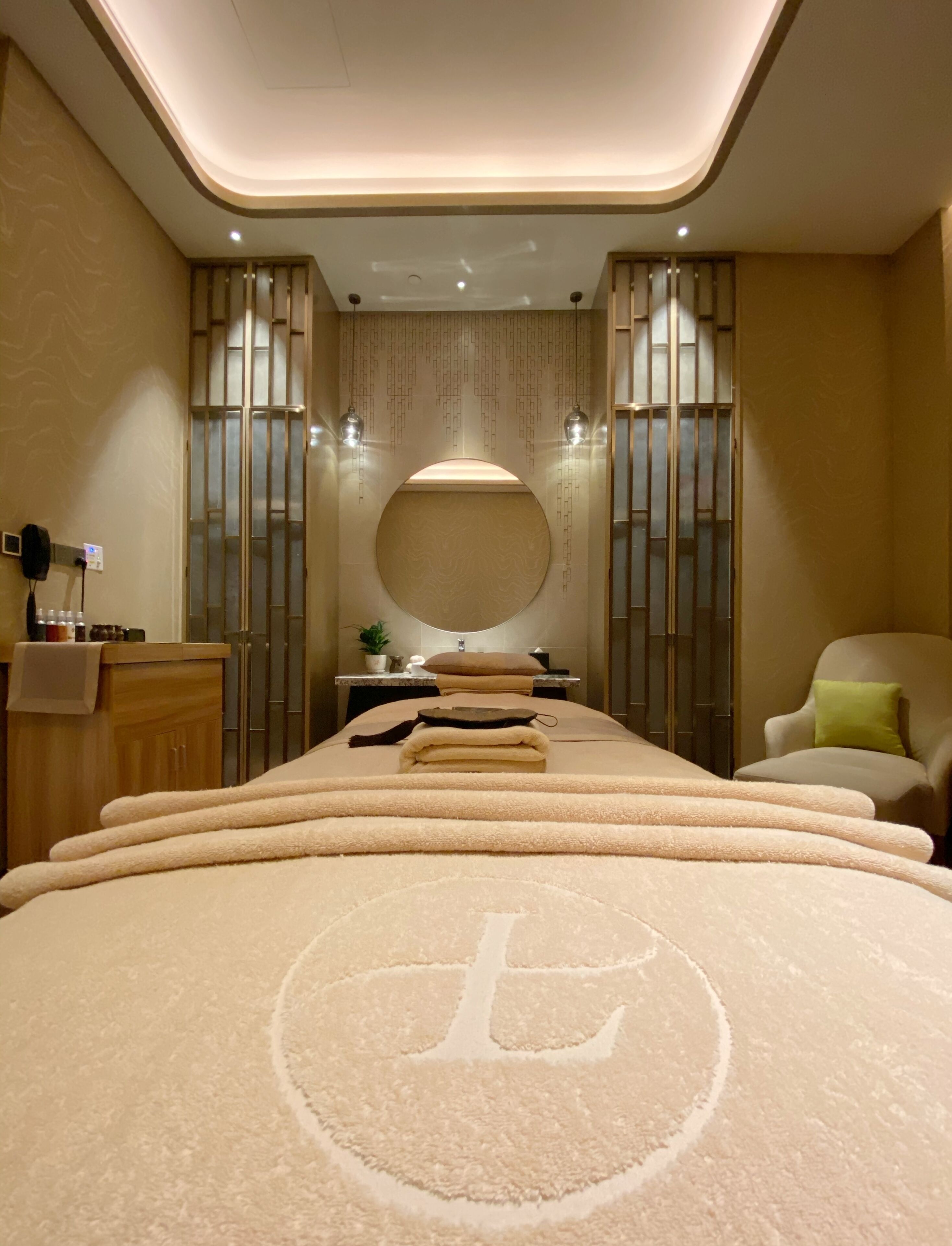 A modern spa room with a large bed, a round mirror, and a seating area.