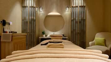 A modern spa room with a large bed, a round mirror, and a seating area.