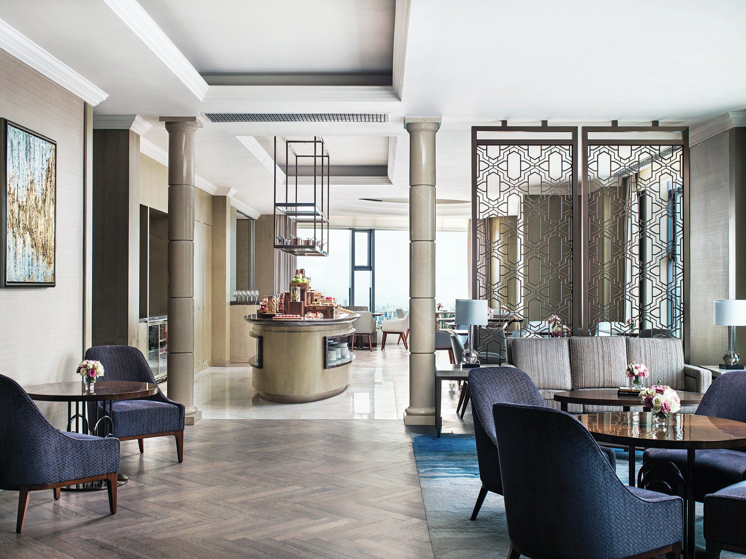 A spacious hotel lobby with a central bar, seating areas, and a decorative partition.