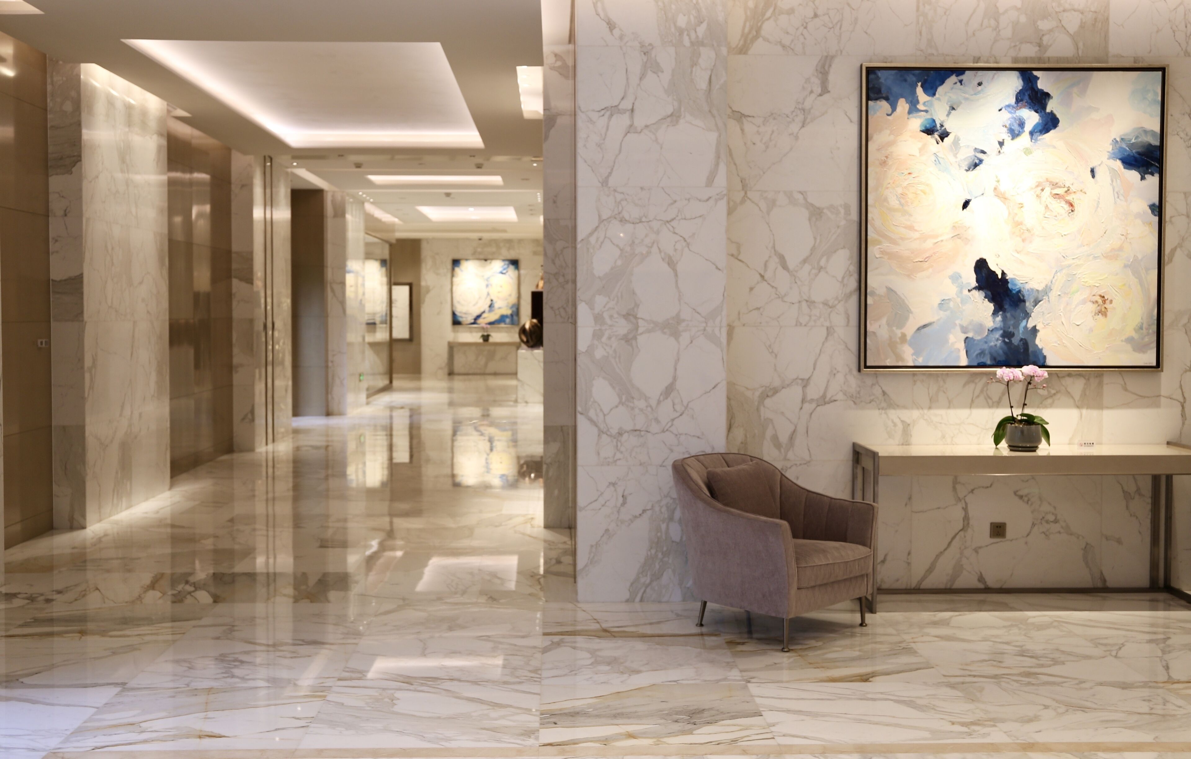 Un hall de hotel con piso de mármol, una recepción, una silla y arte abstracto en la pared.