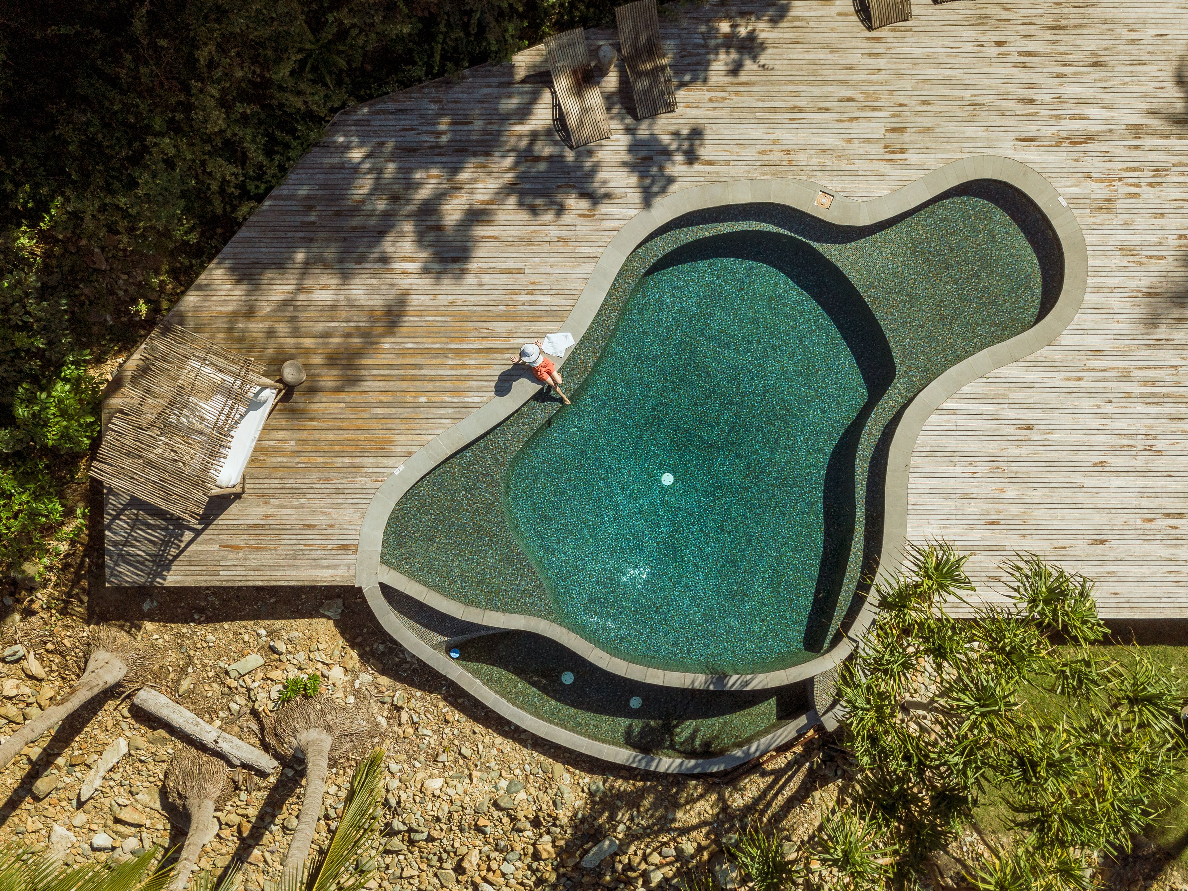 Vista aérea de uma piscina com formato peculiar e deck de madeira ao redor.