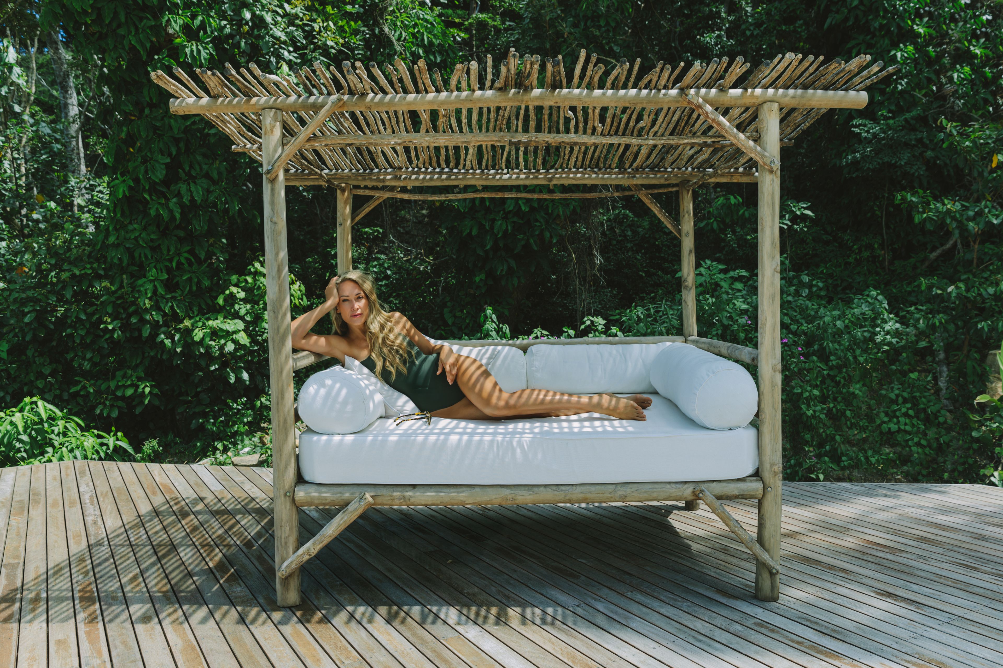 A wooden deck with a white cushioned outdoor seating area under a bamboo pergola.