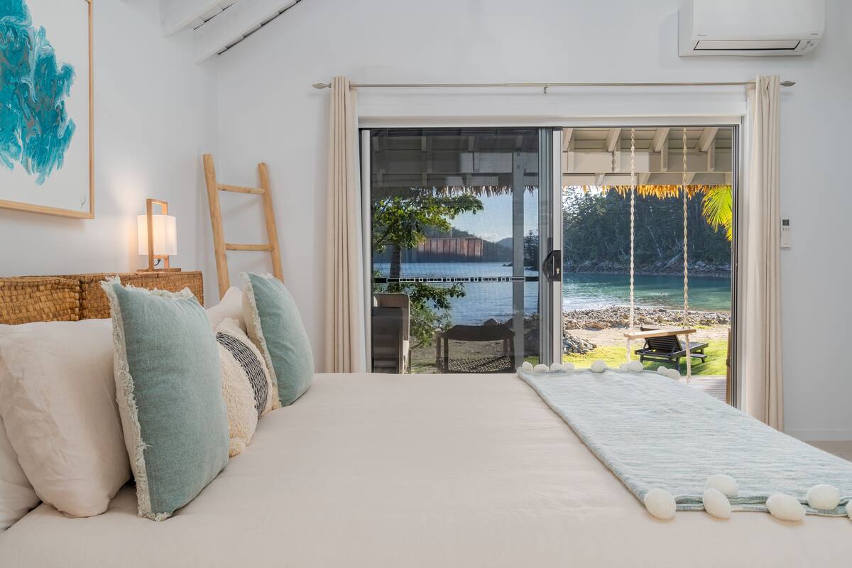 Quarto com cama grande, vista para a praia e escada de madeira.