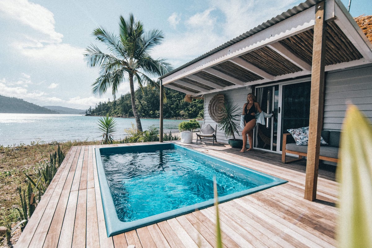 Um deck de madeira com piscina, varanda coberta e vista para o mar.