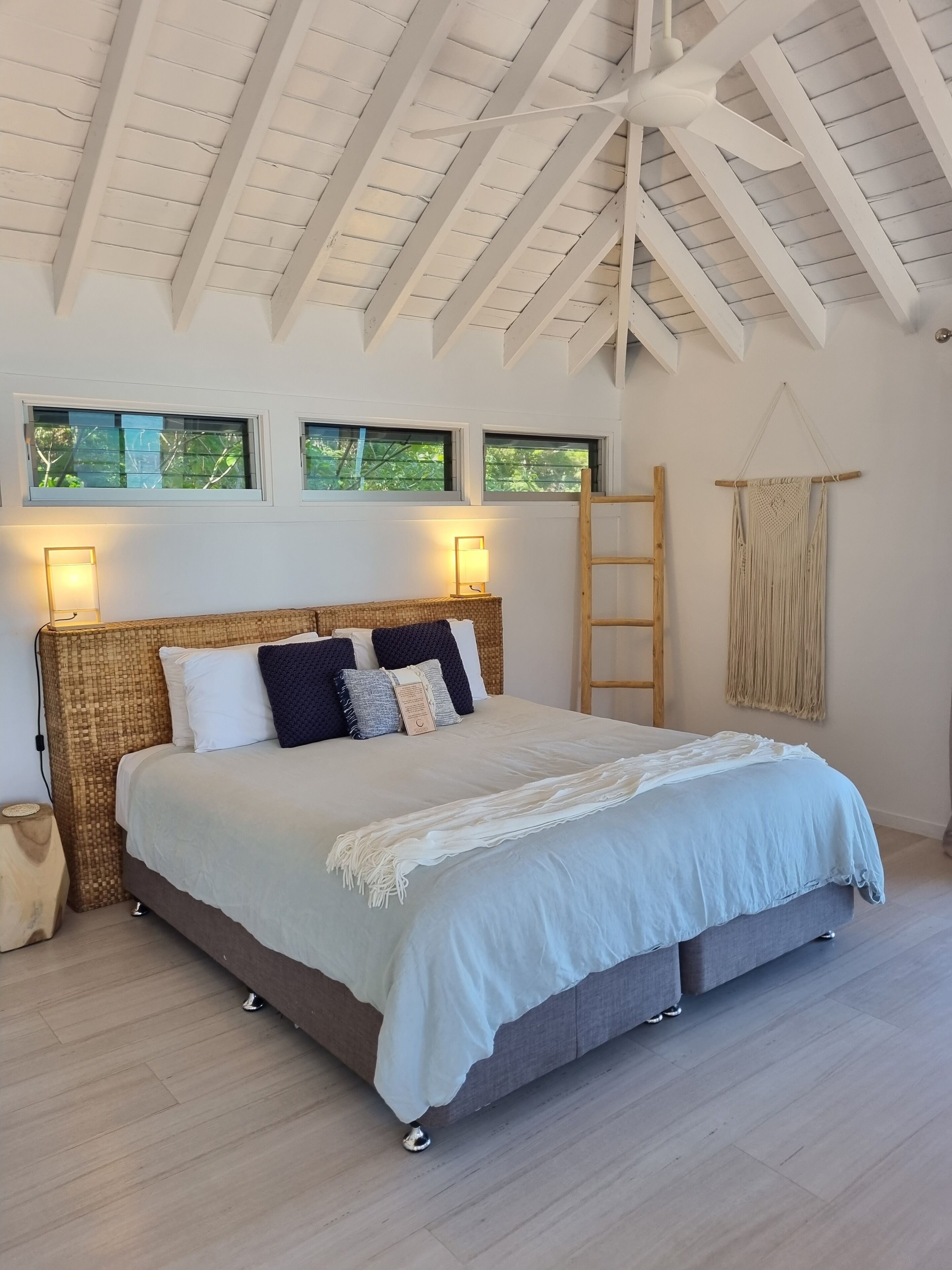 Une chambre à coucher avec un lit, des lampes de chevet, une échelle et une décoration murale en macramé.