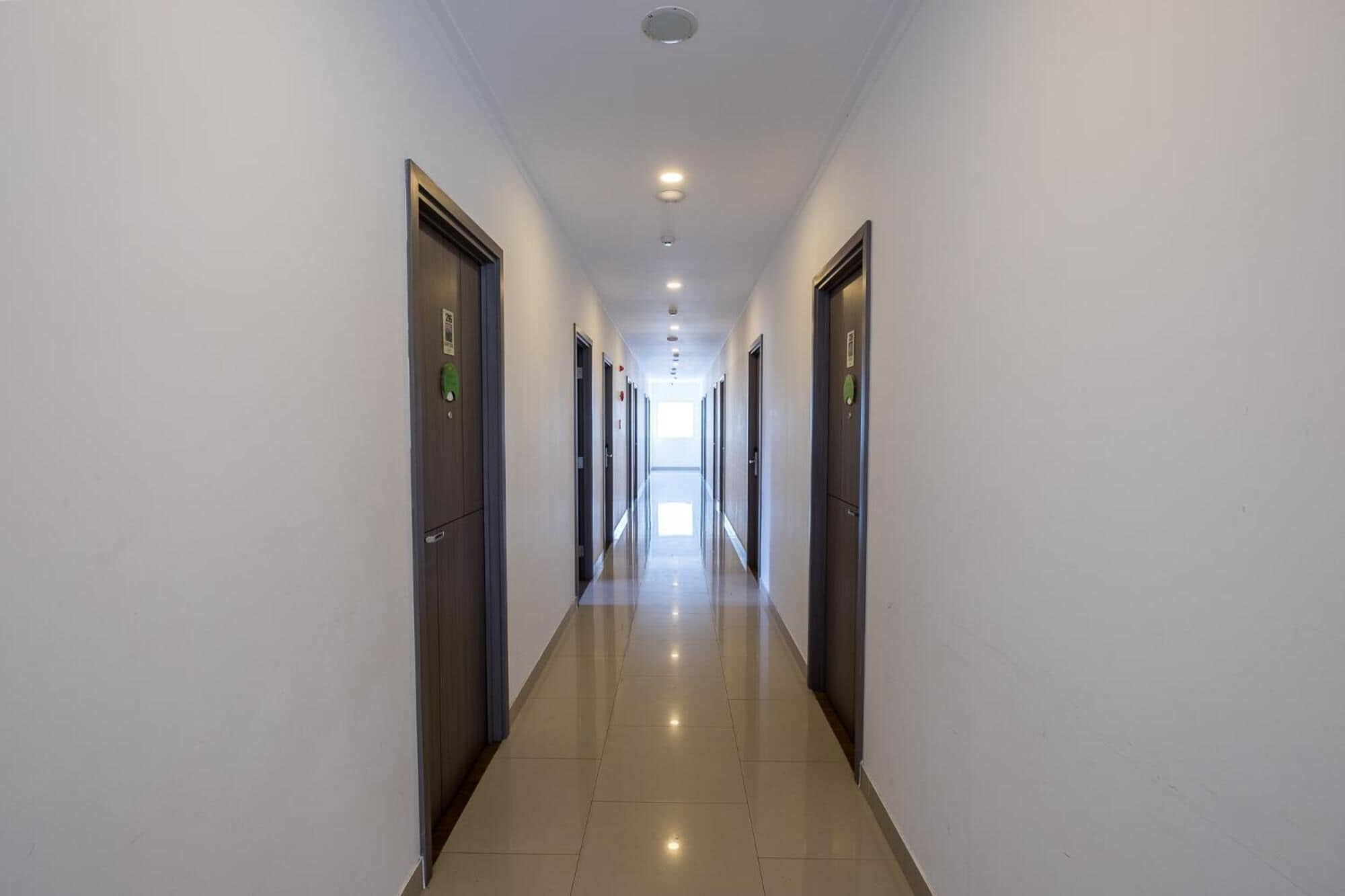Un pasillo largo y estrecho con puertas a ambos lados, que conduce a un espacio luminoso al final.