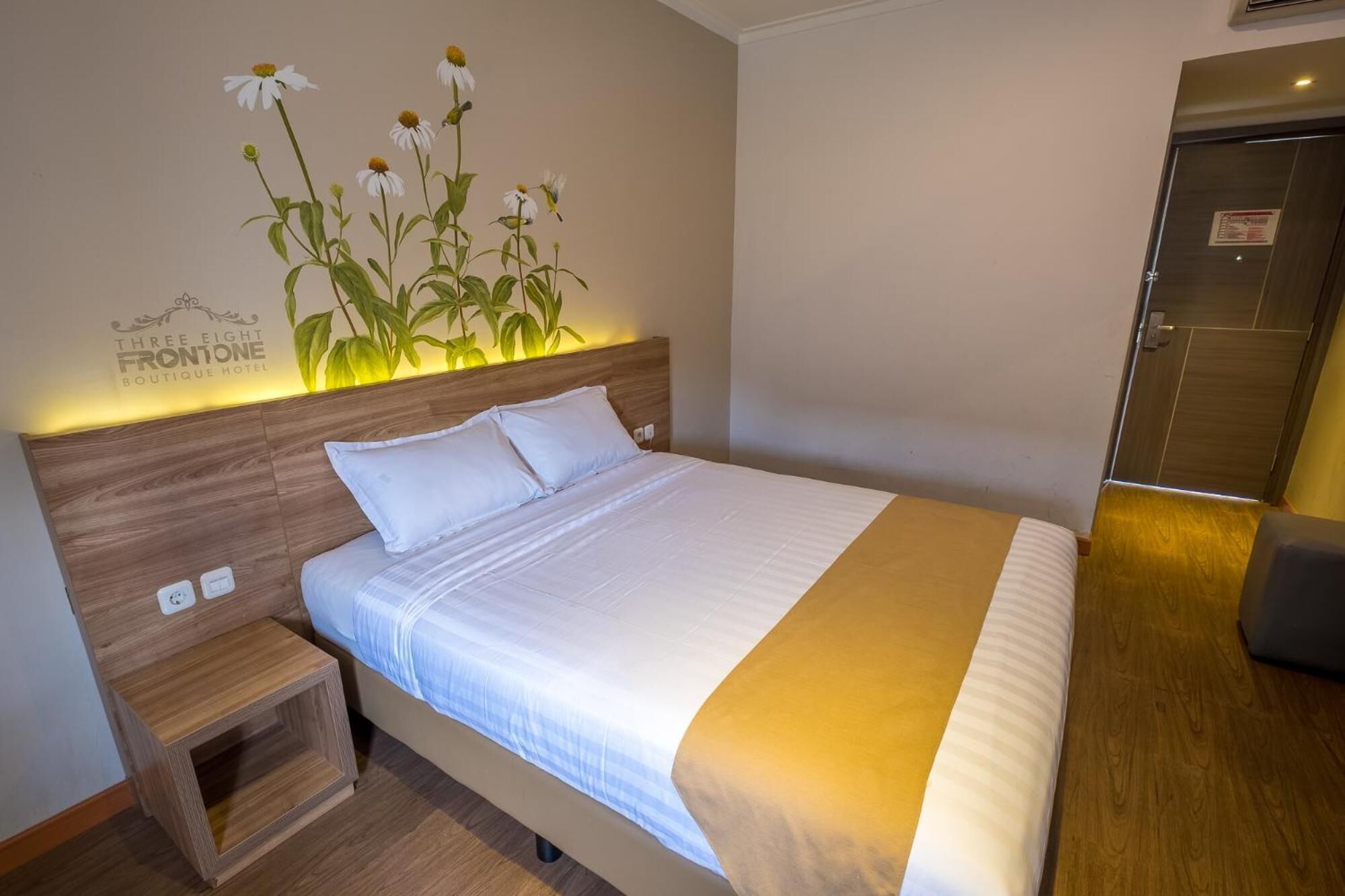 A hotel room with a bed, bedside tables, a wall-mounted artwork, and a door.
