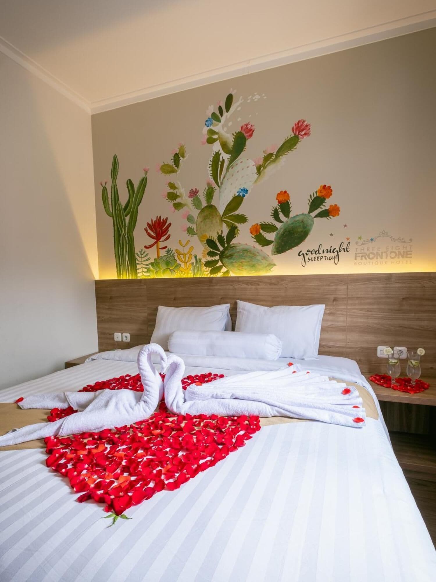 Ein Hotelzimmer mit einem Bett, weißen Leinen, einem Wandbild mit Kakteen und Blumen sowie einem Schild mit der Aufschrift 'good night sleep tight'.