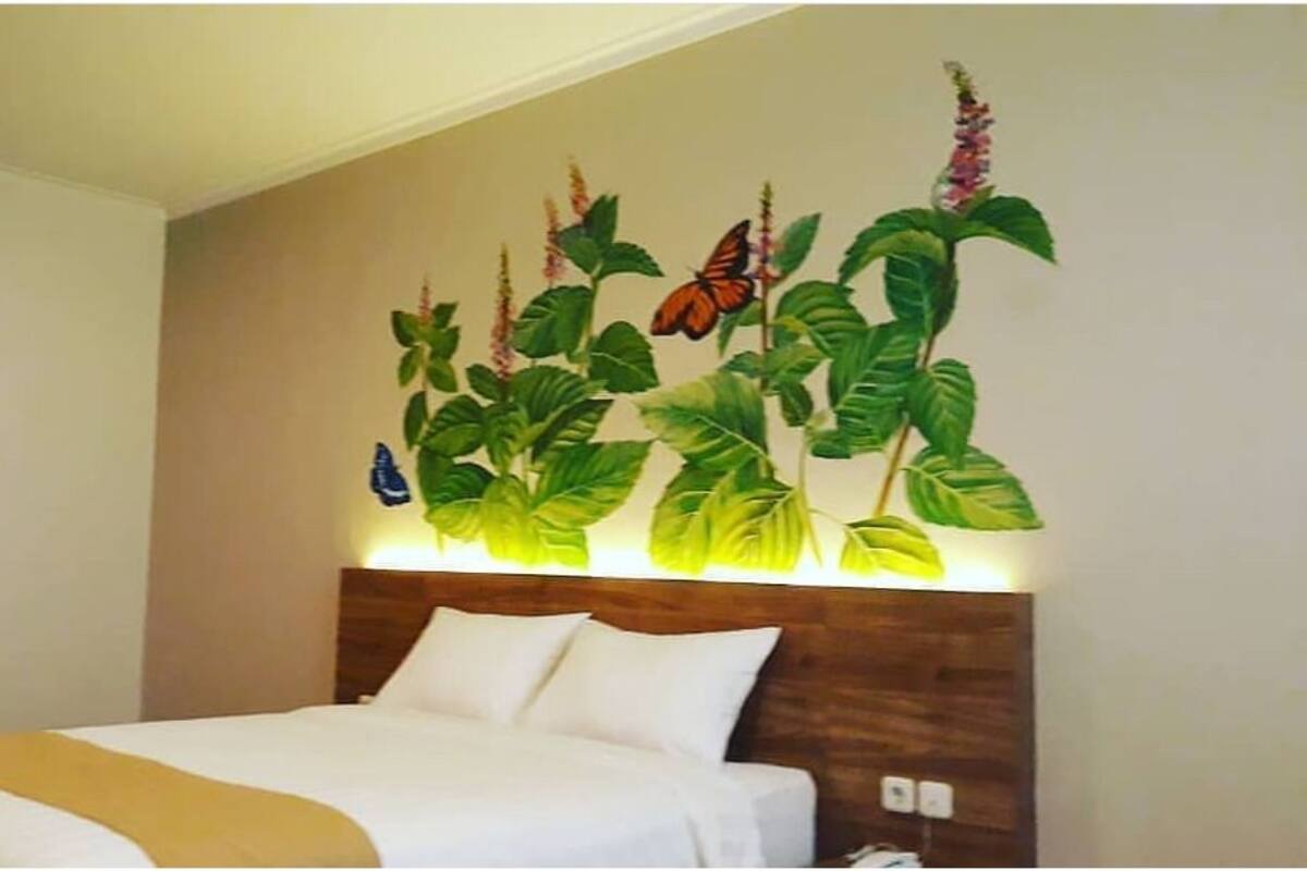 A hotel room with a bed, a headboard, and a wall mural of plants and butterflies.
