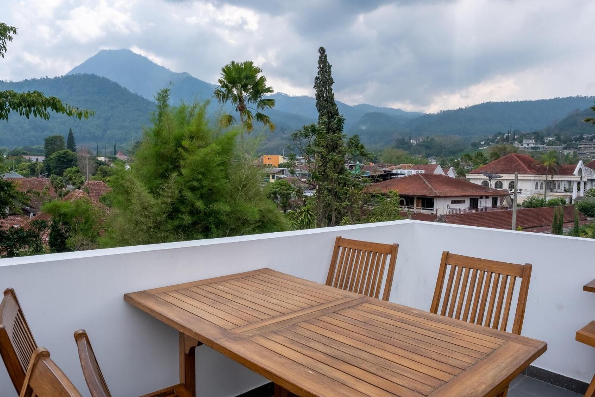 A wooden table and chairs on a balcony with a view of a town and mountains in the background.