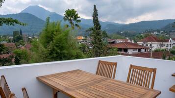 A wooden table and chairs on a balcony with a view of a town and mountains in the background.