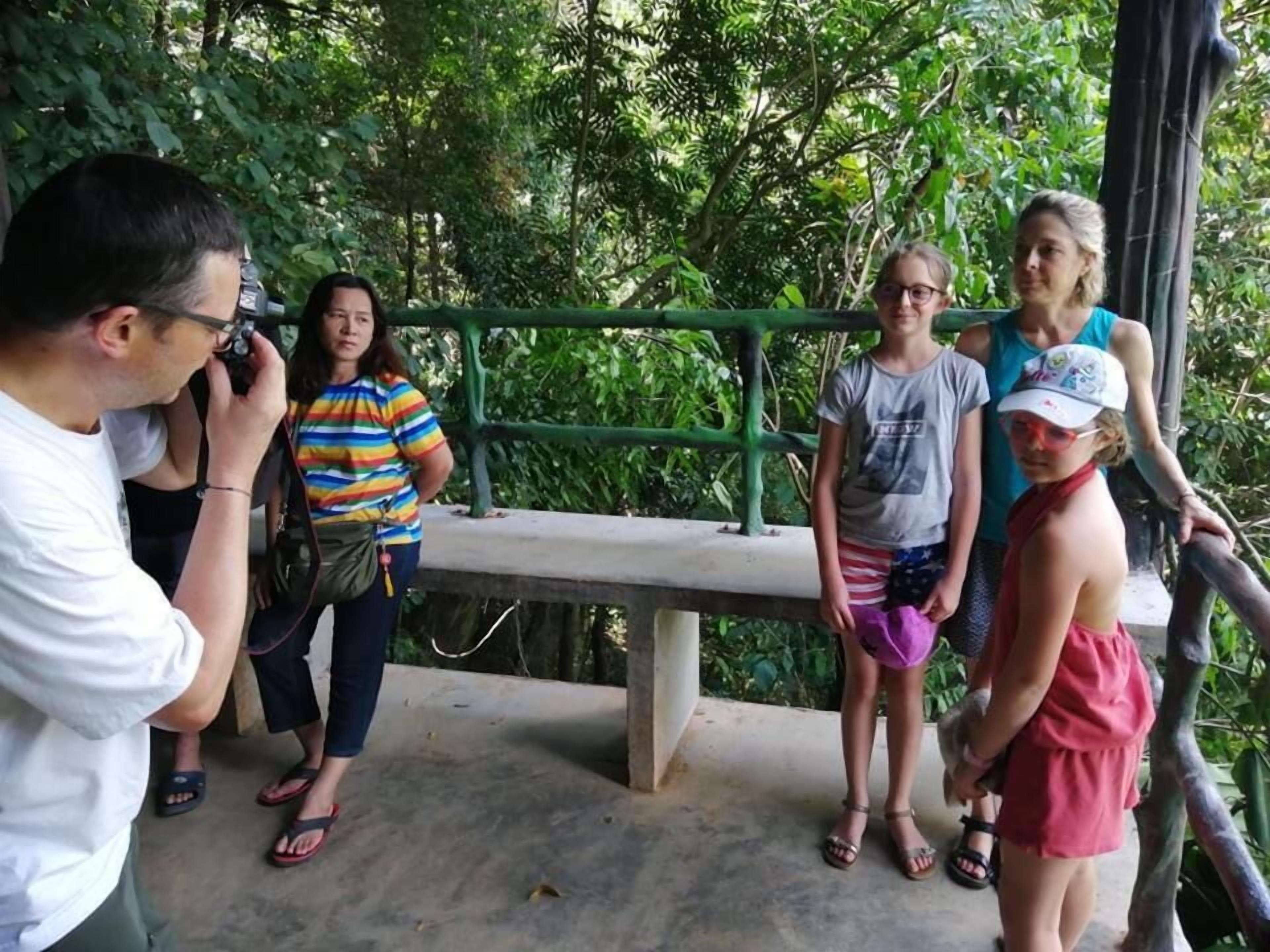 A group of people standing on a concrete platform with a green railing, surrounded by lush greenery.
