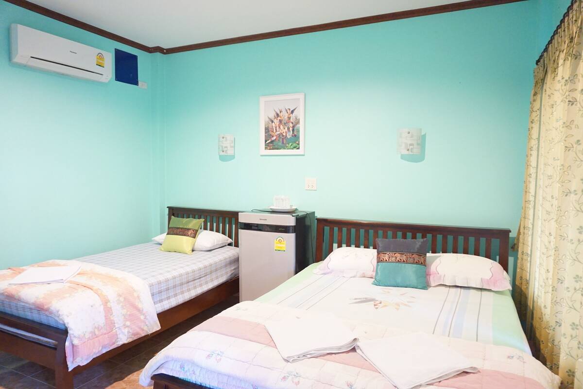 Una habitación con dos camas individuales, aire acondicionado, un refrigerador pequeño y un interruptor de luz en la pared.