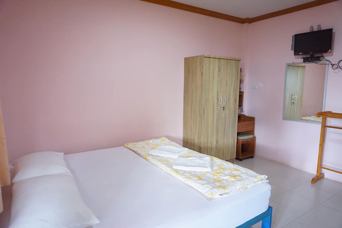 Una cama bien hecha con colcha estampada y almohadas blancas, un armario de madera, un televisor montado en la pared y una pequeña mesa de madera.