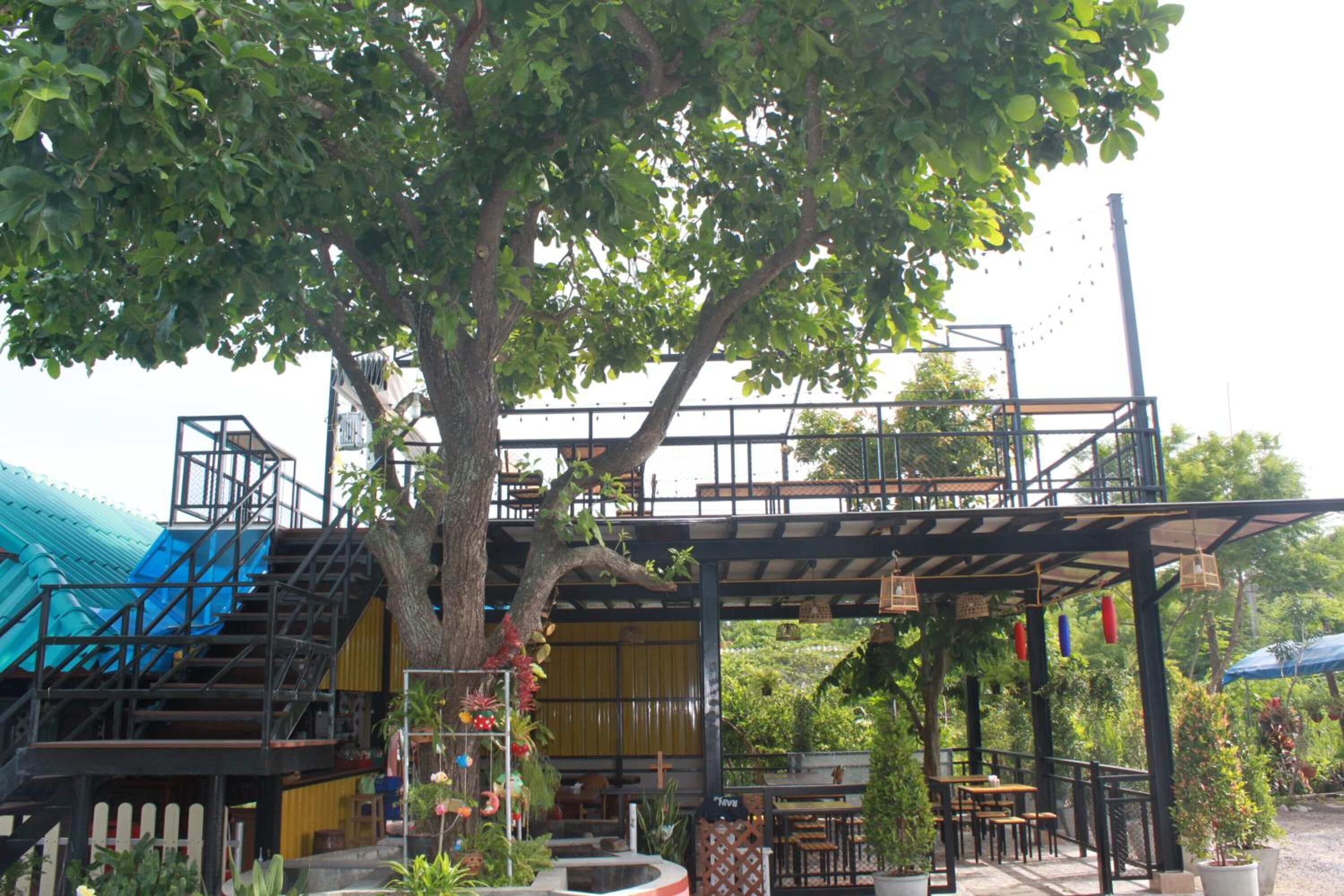 A covered outdoor seating area with tables and chairs, a staircase, and a tree providing shade.