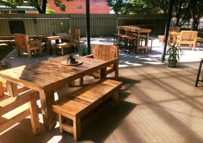 An outdoor patio area with wooden tables and chairs, a concrete floor, and a brick wall in the background. - Riverina Hotel (Holbrook)