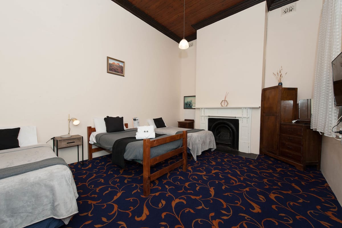 Habitación de hotel con dos camas, chimenea, armario de madera y alfombra estampada.