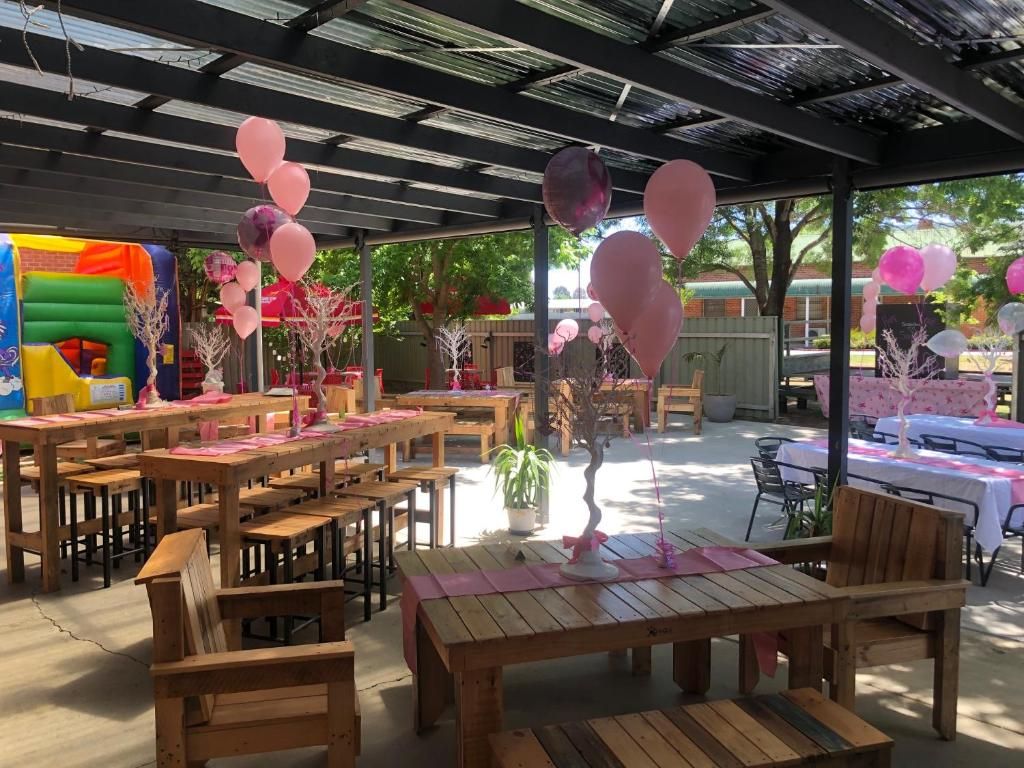 An outdoor patio area with wooden tables and chairs, balloons, and a play structure.