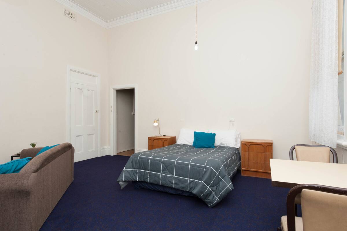 Una habitación de hotel con cama, escritorio, silla, mesita de noche y puerta.