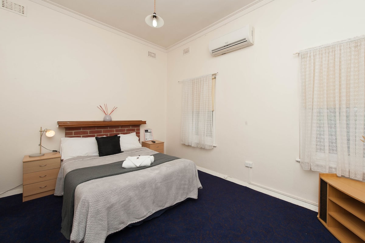 Habitación de hotel ordenada con cama, mesita de noche, lámpara y ventana con cortinas.