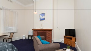 A living room with a sofa, a small table with a plant, a television, and a fireplace. - Riverina Hotel (Holbrook)