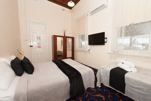 A hotel room with two beds, a TV, a mirror, and a window with a view. - Riverina Hotel (Holbrook)