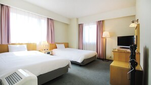 Habitación de hotel con dos camas, un escritorio, un televisor y una lámpara.