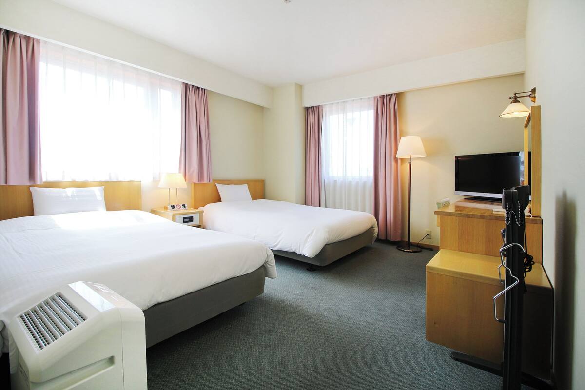 Ein Hotelzimmer mit zwei Betten, einem Schreibtisch, einem Fernseher und einer Lampe.