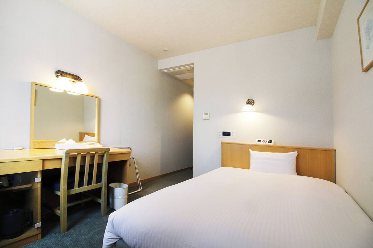 Ein Hotelzimmer mit einem Bett, einem Schreibtisch mit Stuhl, einem Spiegel und einem Nachttisch.