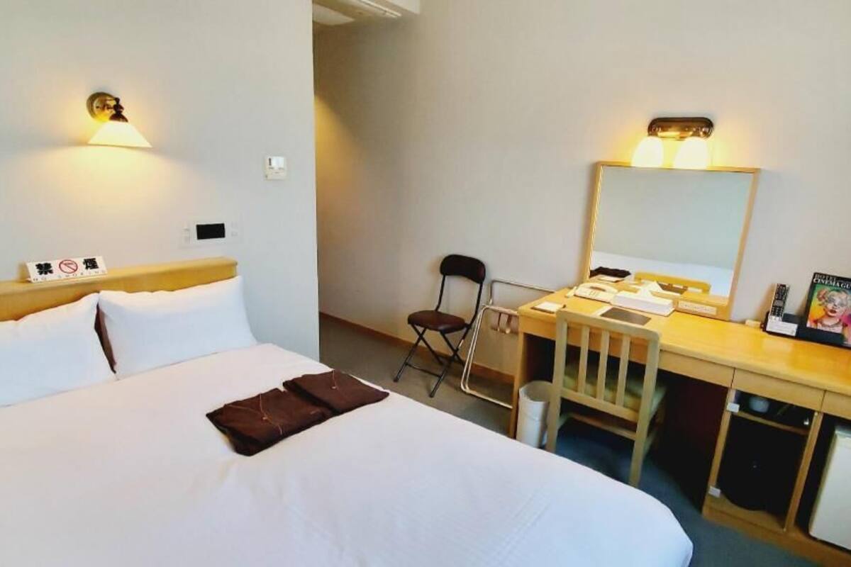 Ein Hotelzimmer mit Bett, Schreibtisch mit Stuhl, Spiegel und Nachttisch.