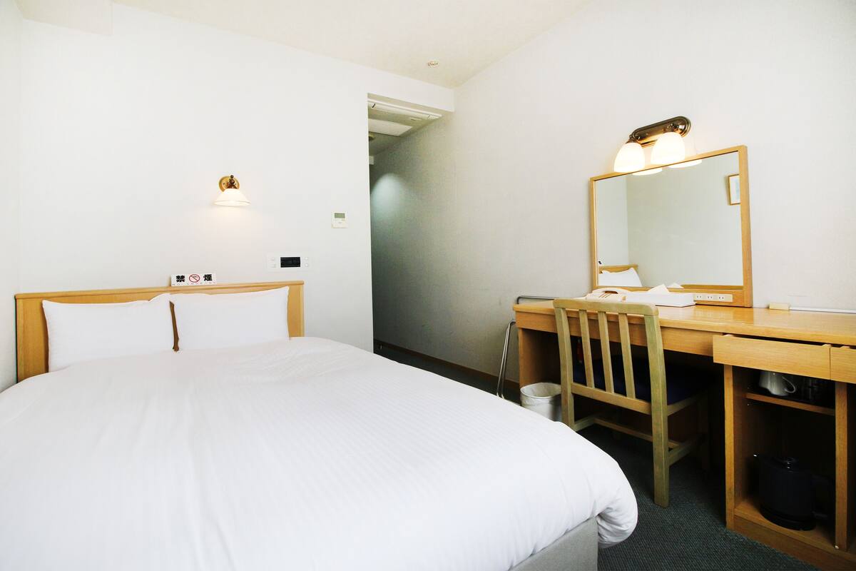 Ein Hotelzimmer mit einem großen Bett, einem Holztisch, einem Stuhl, einem Spiegel und einer Wandleuchte.