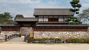 Un edificio tradicional japonés con muro de piedra, puerta de madera y un pequeño puente.