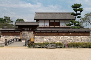A traditional Japanese building with a stone wall, wooden gate, and a small bridge.