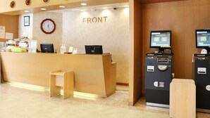Zona de recepción con mostrador de madera, un reloj y un quiosco de autoservicio.