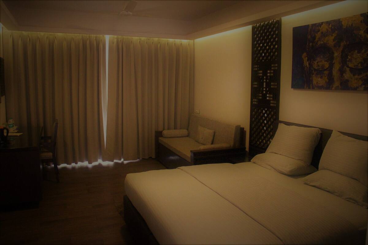 A hotel room with a large bed, a sofa, a desk, and a window with curtains.