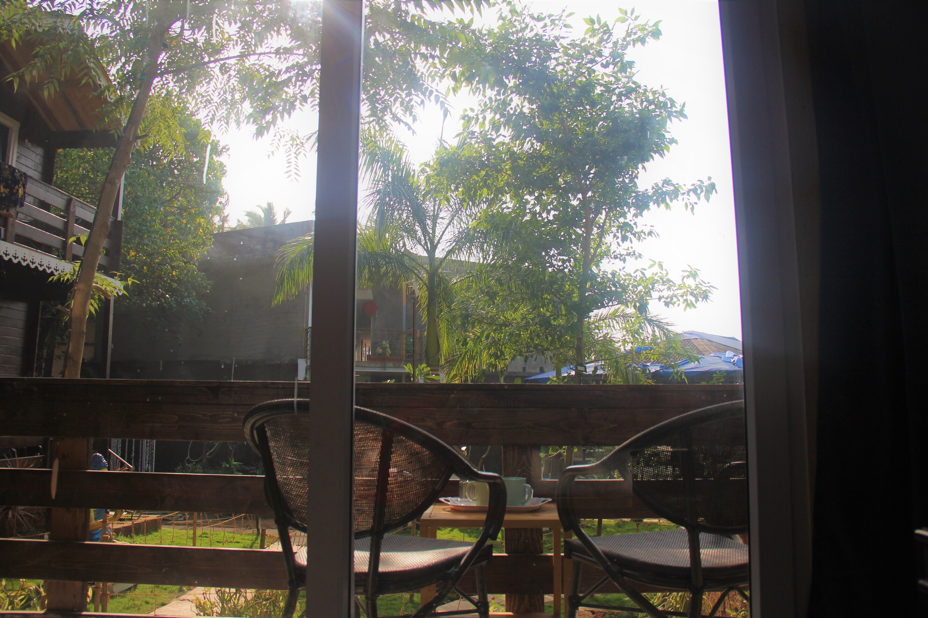 Vista desde una ventana con barandilla de madera, que da a un patio con sillas y una mesa.