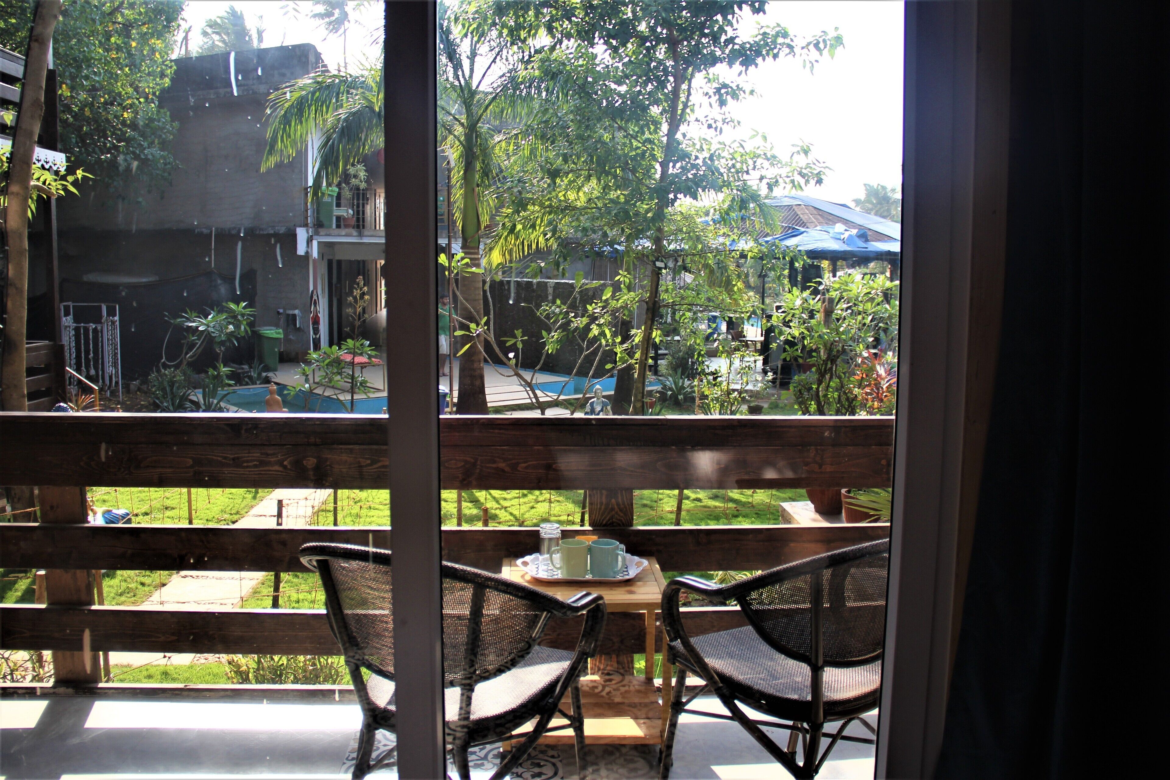 A balcony with wicker chairs and a table, overlooking a garden with a blue umbrella and potted plants.