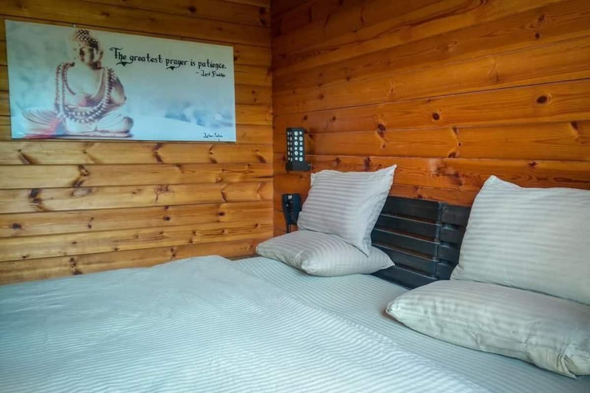 A wooden cabin room with a bed, pillows, a wall-mounted phone, and a poster.