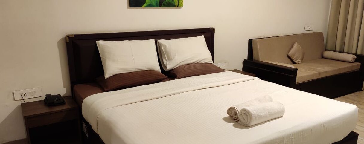 A hotel room with a large bed, two pillows, a bedside table with a phone, and a sofa with cushions.