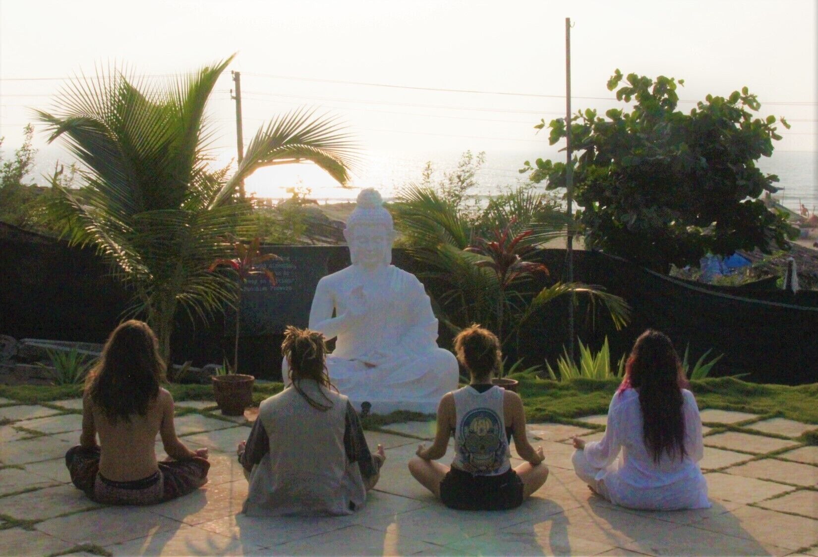 Un grup de persones assegudes en posició meditativa davant d'una gran estàtua blanca.