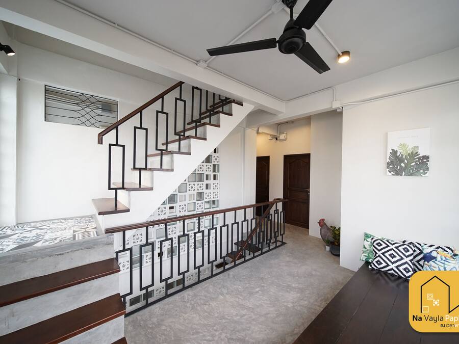 A modern interior with a staircase, ceiling fan, and a sofa with patterned cushions.