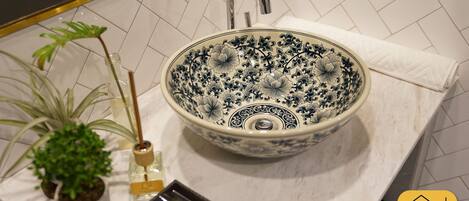 A bathroom with a decorative ceramic sink, a potted plant, and a towel on the counter.