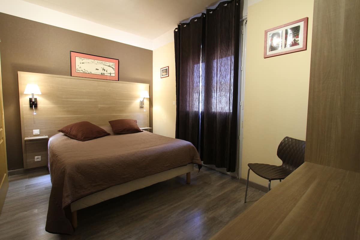 A hotel room with a large bed, two bedside lamps, a chair, and a window with curtains.