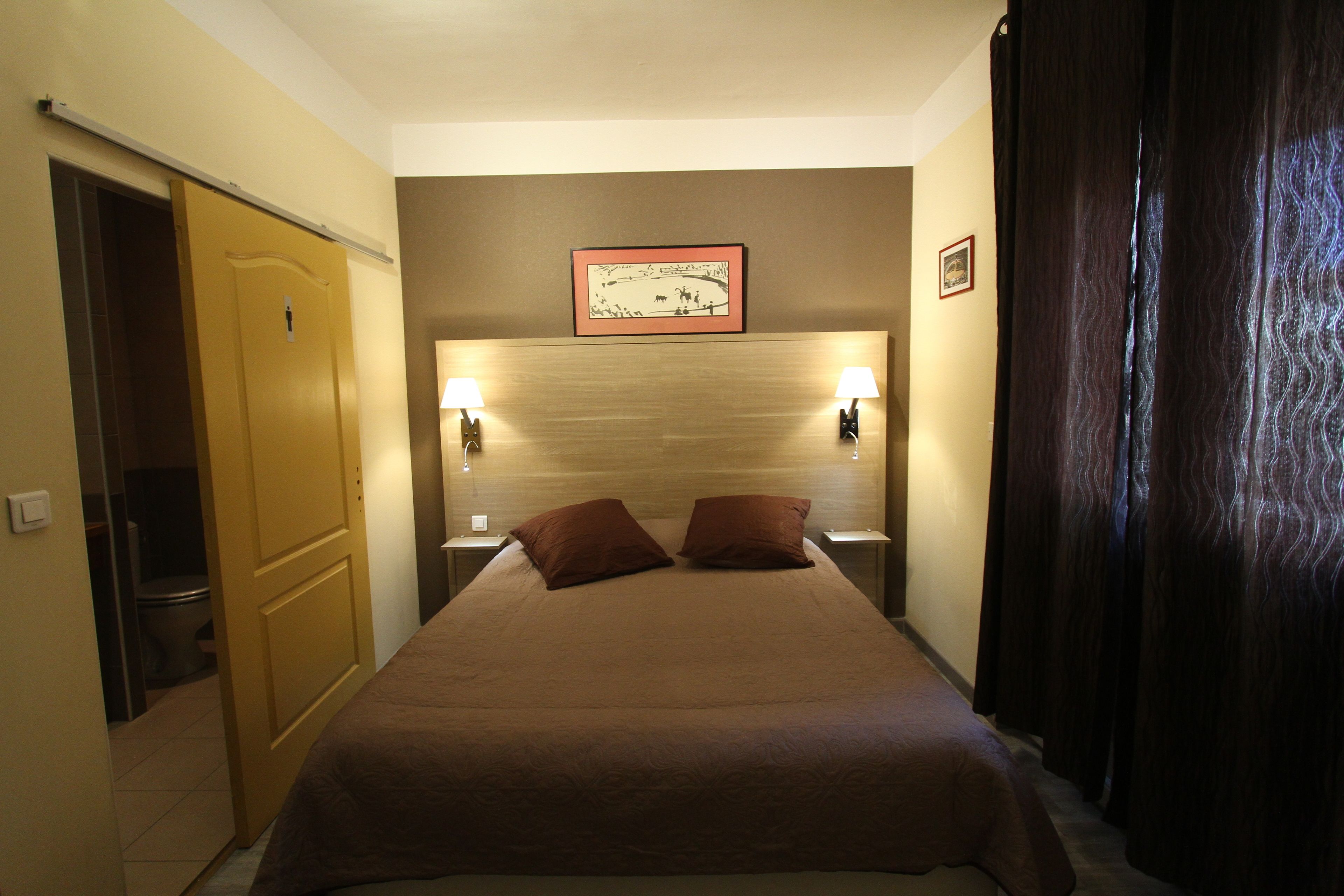 Une chambre d’hôtel avec un lit, deux lampes de chevet, une tête de lit, une porte et un tableau encadré au mur.
